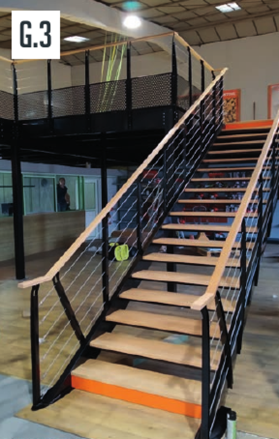 Schody industrialne prowadzące na antresolę z drewnianymi stopniami i linową balustradą