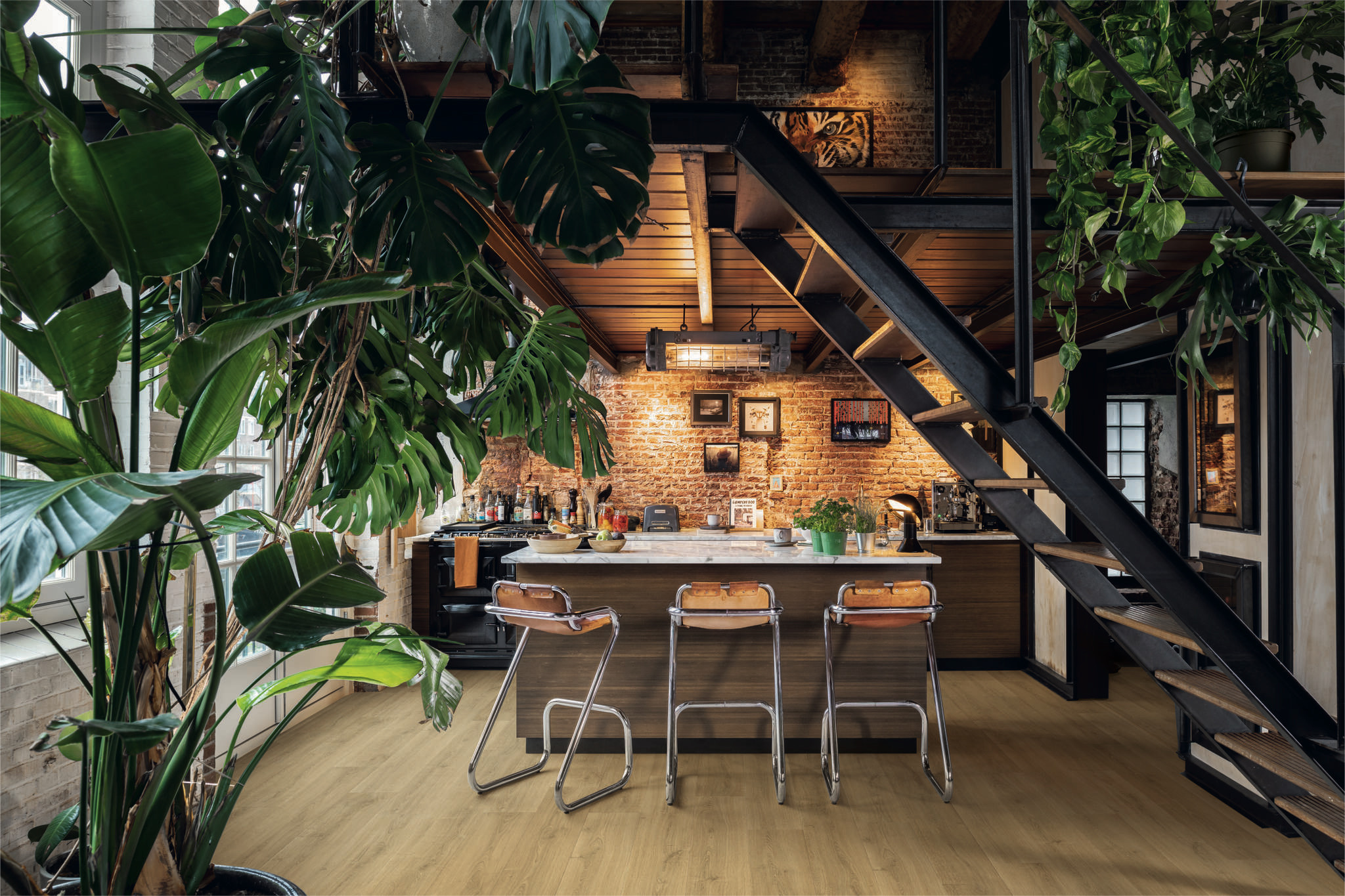 Nowoczesna kuchnia w stylu industrialnym z ceglaną ścianą, czarnymi metalowymi schodami, drewnianą podłogą, wyspą kuchenną z hokerami oraz dużymi roślinami monstera. trendy w regałach biurowych