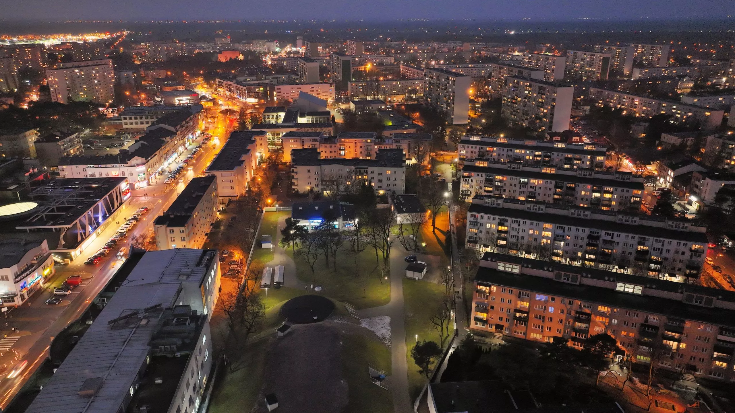 Nocna panorama Legionowa z lotu ptaka, oświetlone osiedla mieszkaniowe, główna arteria miasta i park miejski w centrum kadru. Regały Magazynowe w Legionowie
