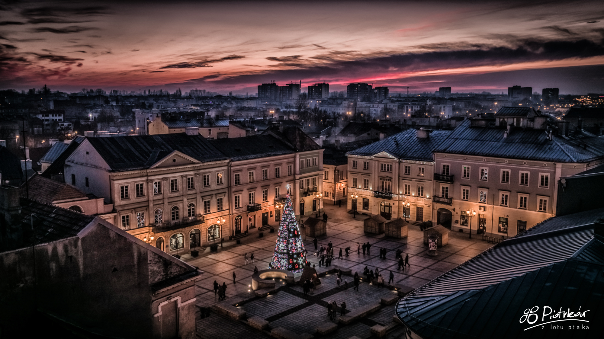Rynek Trybunalski w Piotrkowie o zmierzchu, oświetlona choinka świąteczna, zabytkowe kamienice i różowe niebo nad miastem. Regały Magazynowe Piotrków Trybunalski